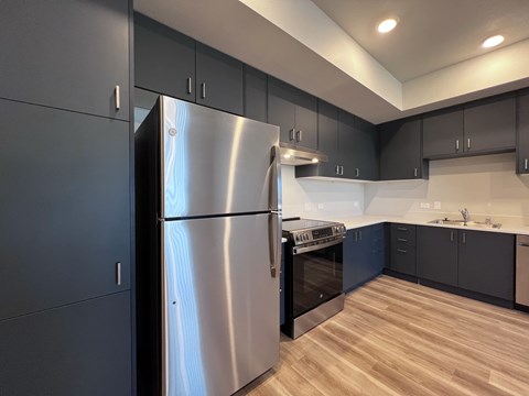 A modern kitchen with a stainless steel refrigerator and wooden flooring.