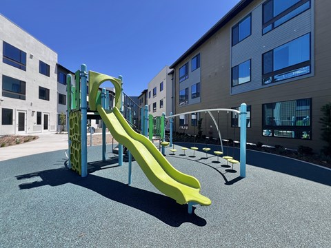 A playground with a yellow slide in front of a building.