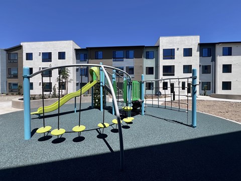 A playground with a green slide and yellow and black swings.
