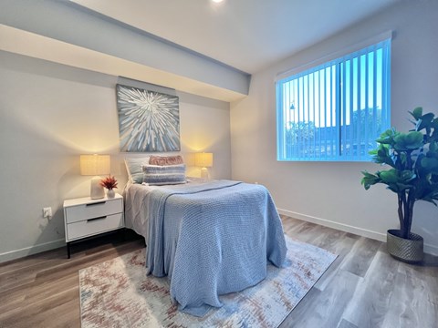 A bedroom with a bed, nightstand, and a potted plant.