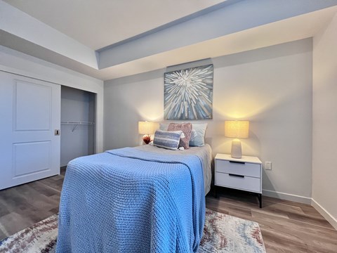 A bedroom with a bed covered in a blue blanket and a white nightstand with a lamp.