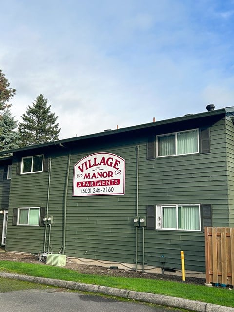 A green building with a sign that says Village Manor Apartments.
