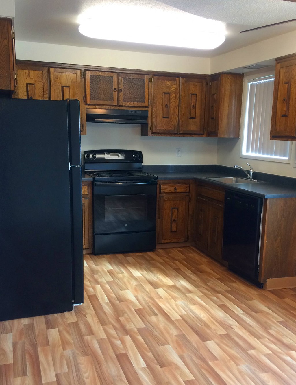 an empty kitchen with wooden flooring and black appliances