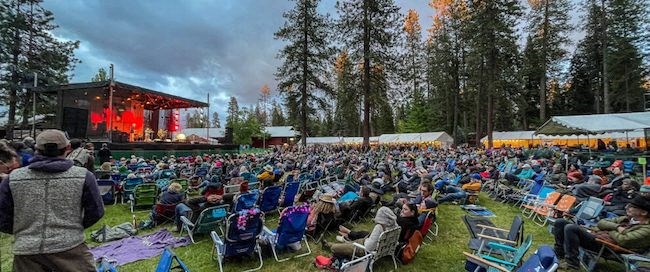 a large crowd of people sitting in lawn chairs in front of a stage