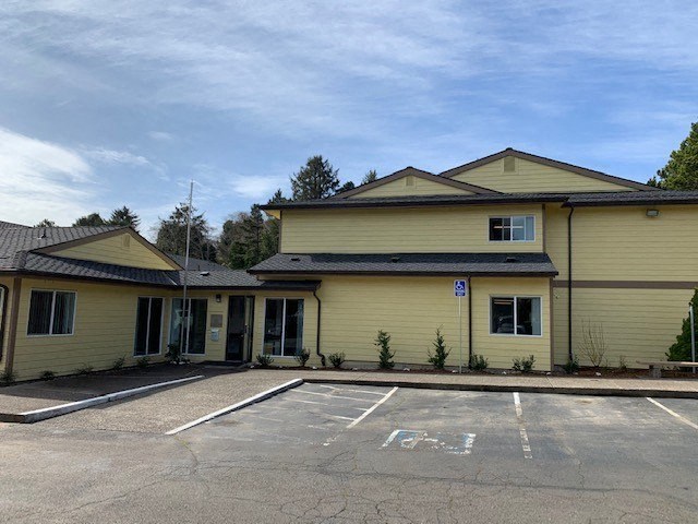 an empty parking lot in front of a yellow house