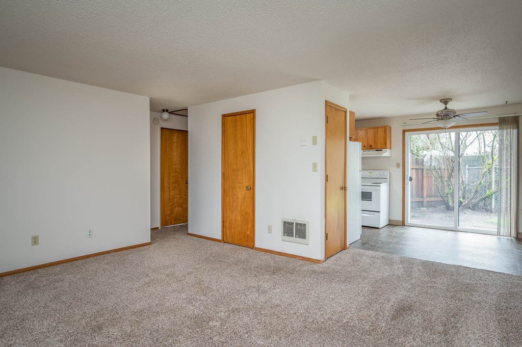 an empty living room with a door leading to a kitchen