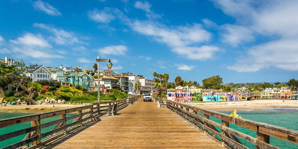A wooden pier leads to a beach with colorful buildings on the shore.