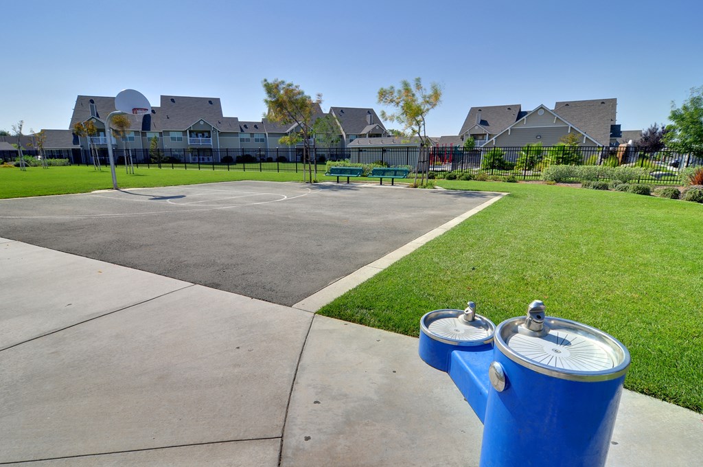 a park with a basketball court and two blue trash cans