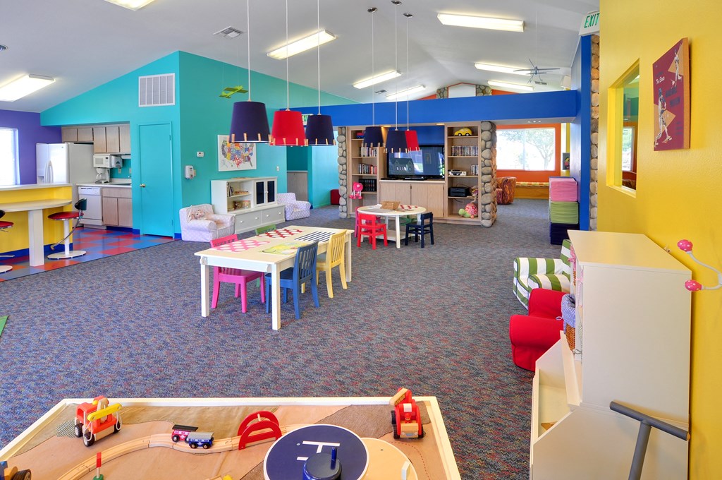 a childrens play area with tables and chairs and a television and kitchen in the background