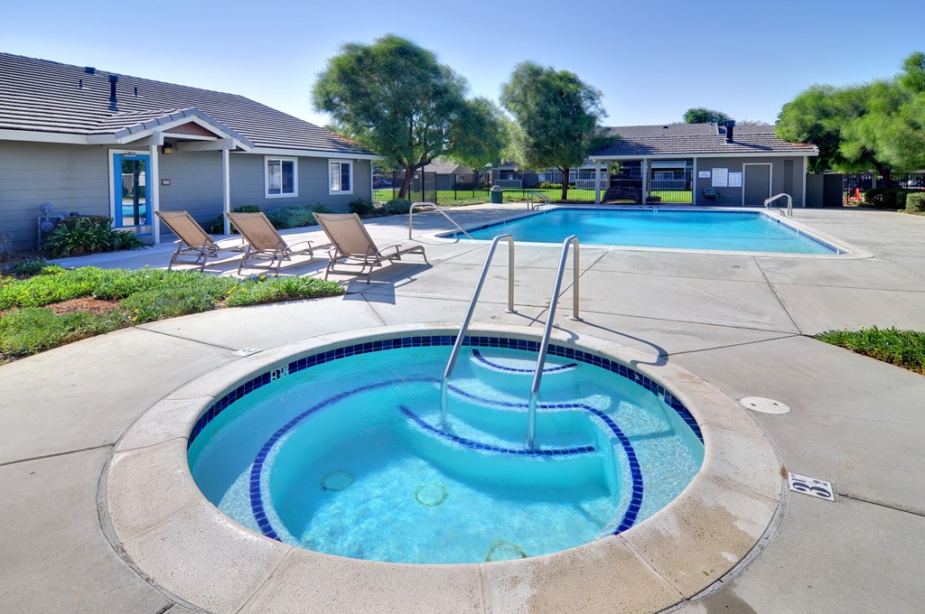 a hot tub with a waterfall in the middle of a concrete patio with lounge chairs and a