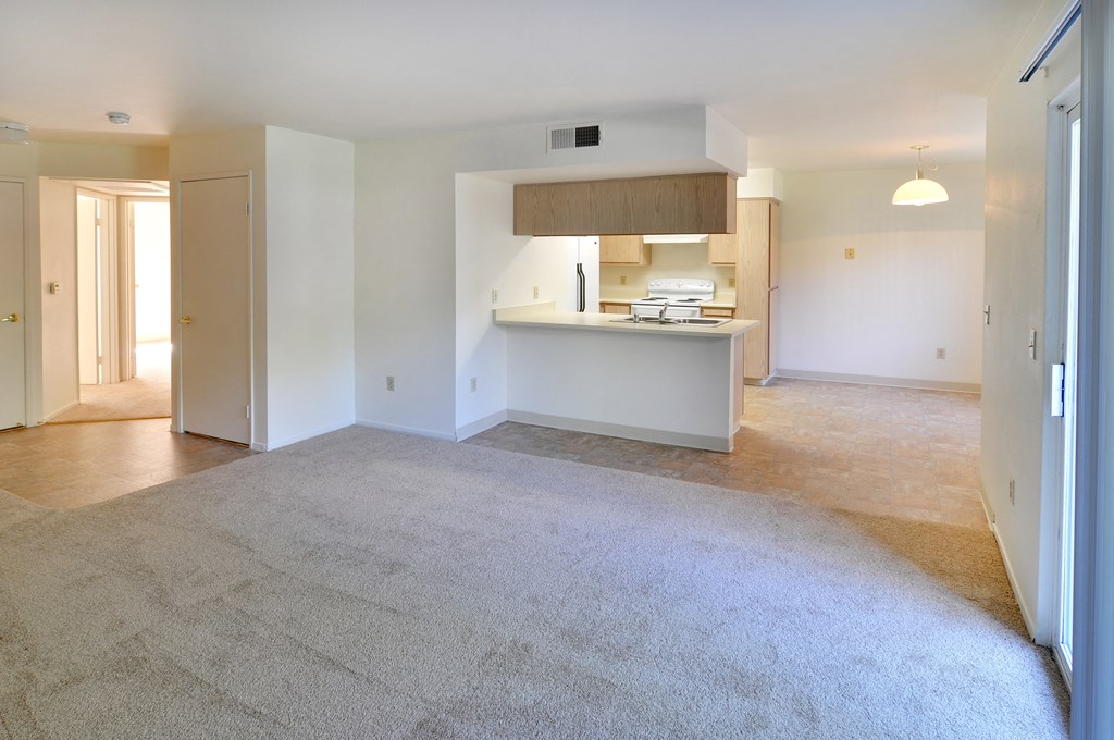 an empty living room with a kitchen in the background