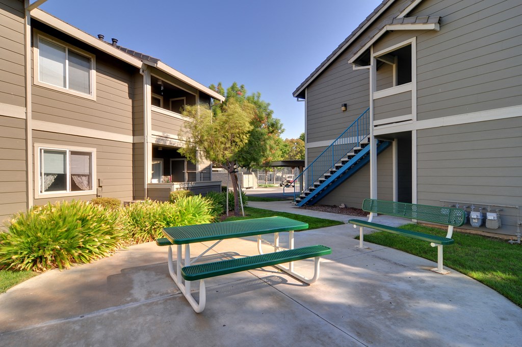 two picnic benches sit in the middle of a concrete patio in front of two apartment buildings