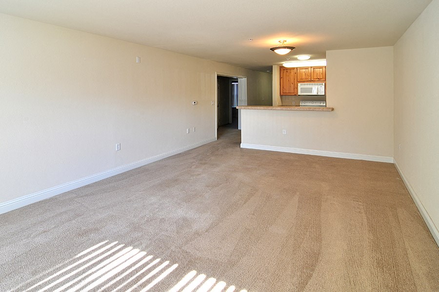 an empty living room with a kitchen in the background