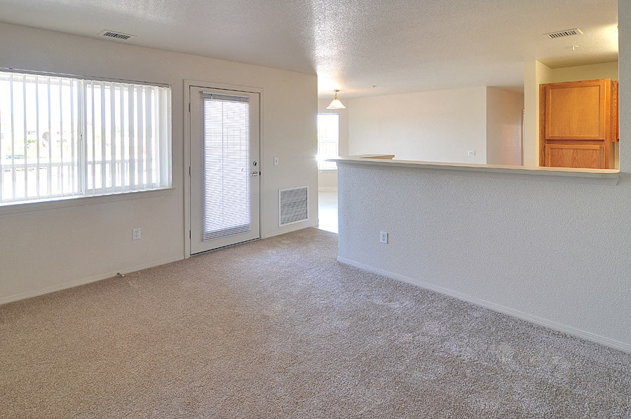an empty living room with a door to a kitchen