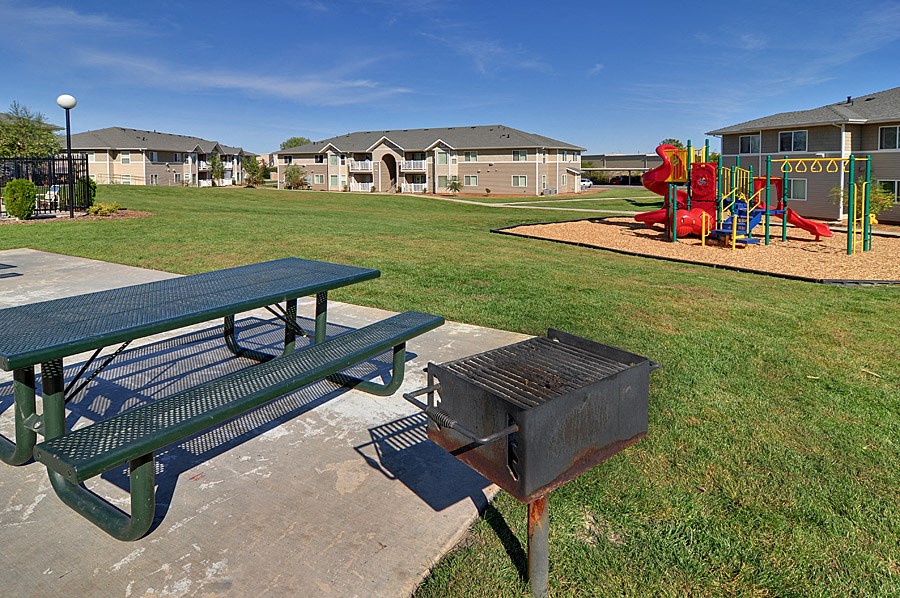 a picnic table and a grill in a park with a playground