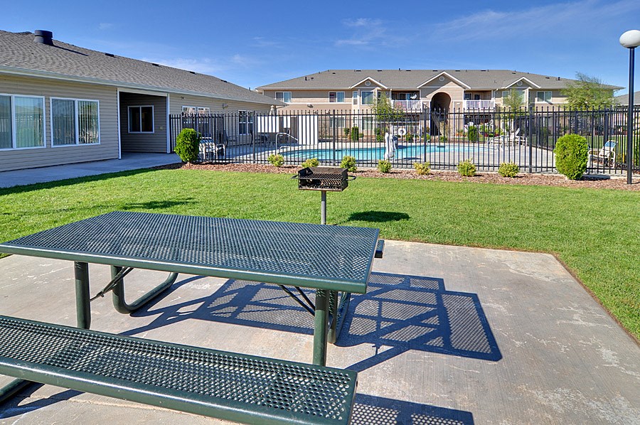 a picnic table with a grill in a yard with a pool