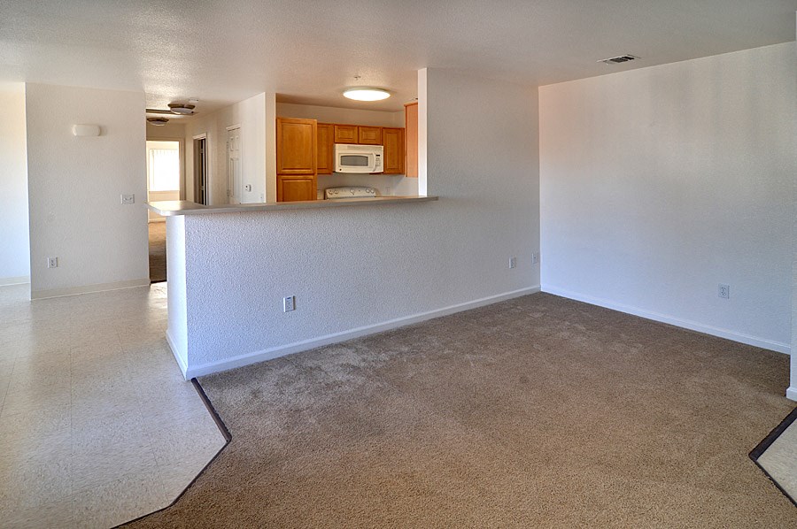 an empty living room with a kitchen in the background