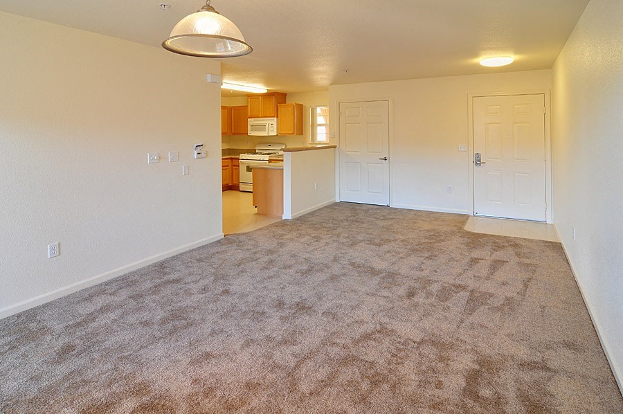 an empty living room with a kitchen in the background