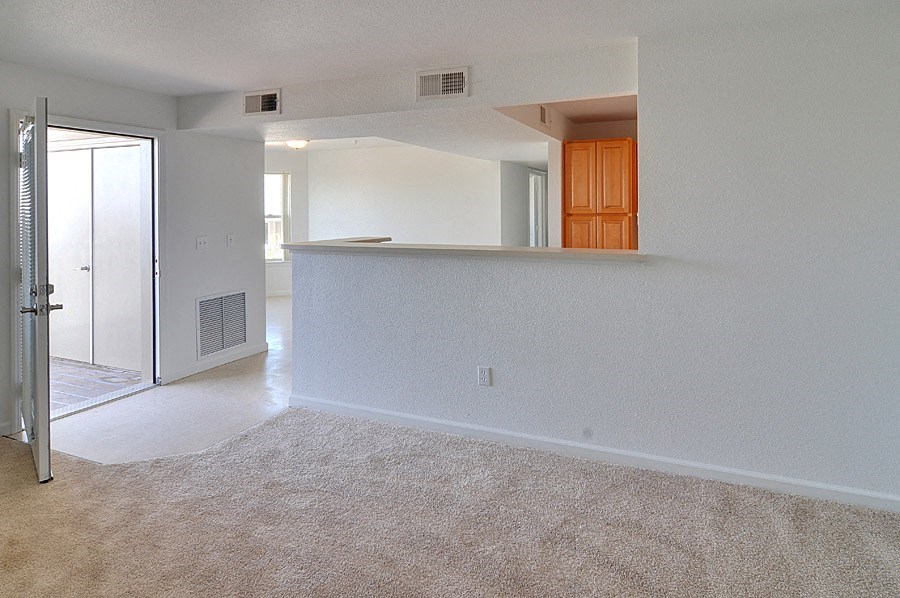 an empty living room with an open door to a kitchen