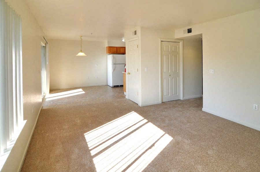 an empty living room with a kitchen in the background