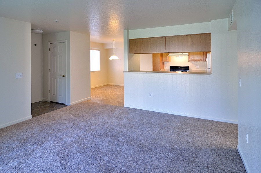 an empty living room with a kitchen in the background