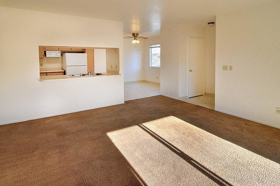an empty living room with a kitchen in the background