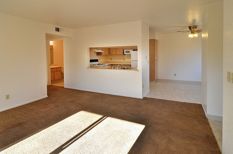 an empty living room with a kitchen in the background