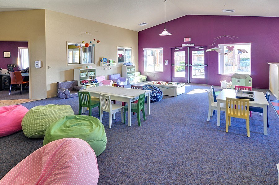 a childrens play room with chairs tables and chairs and a kitchen in the background