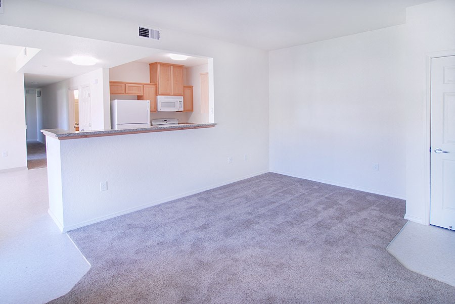 an empty living room with a kitchen in the background