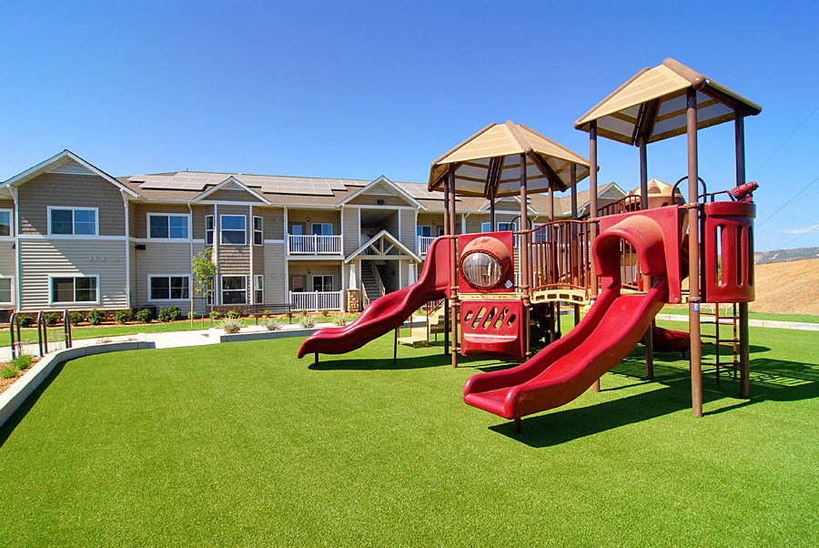 a playground with a red playset in front of an apartment building