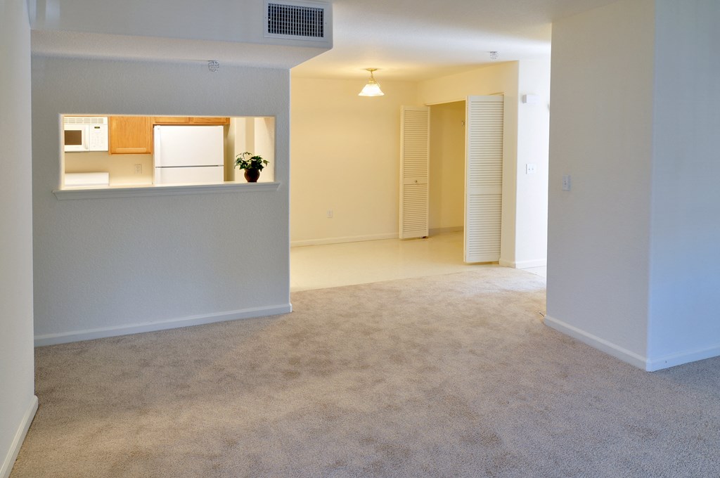 an empty living room with a kitchen in the background