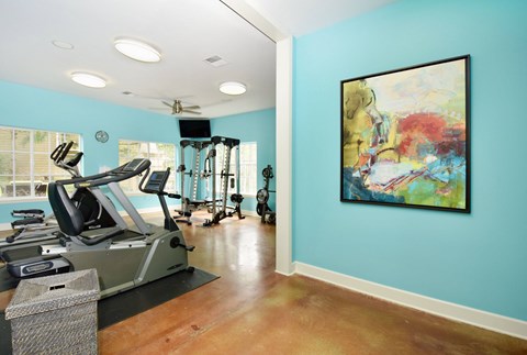 A gym with a treadmill, elliptical machines, and a painting on the wall.