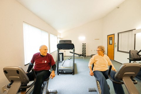Two elderly people exercising in a gym.