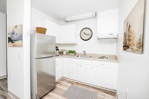 A kitchen with a refrigerator, a clock, and a painting on the wall.