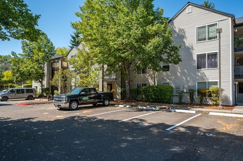 A black pickup truck is parked in a parking lot in front of a two-story apartment building.