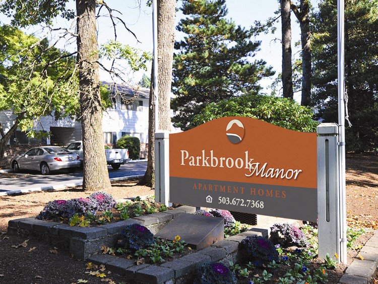 a sign for parkbrook manor in front of trees and flowers