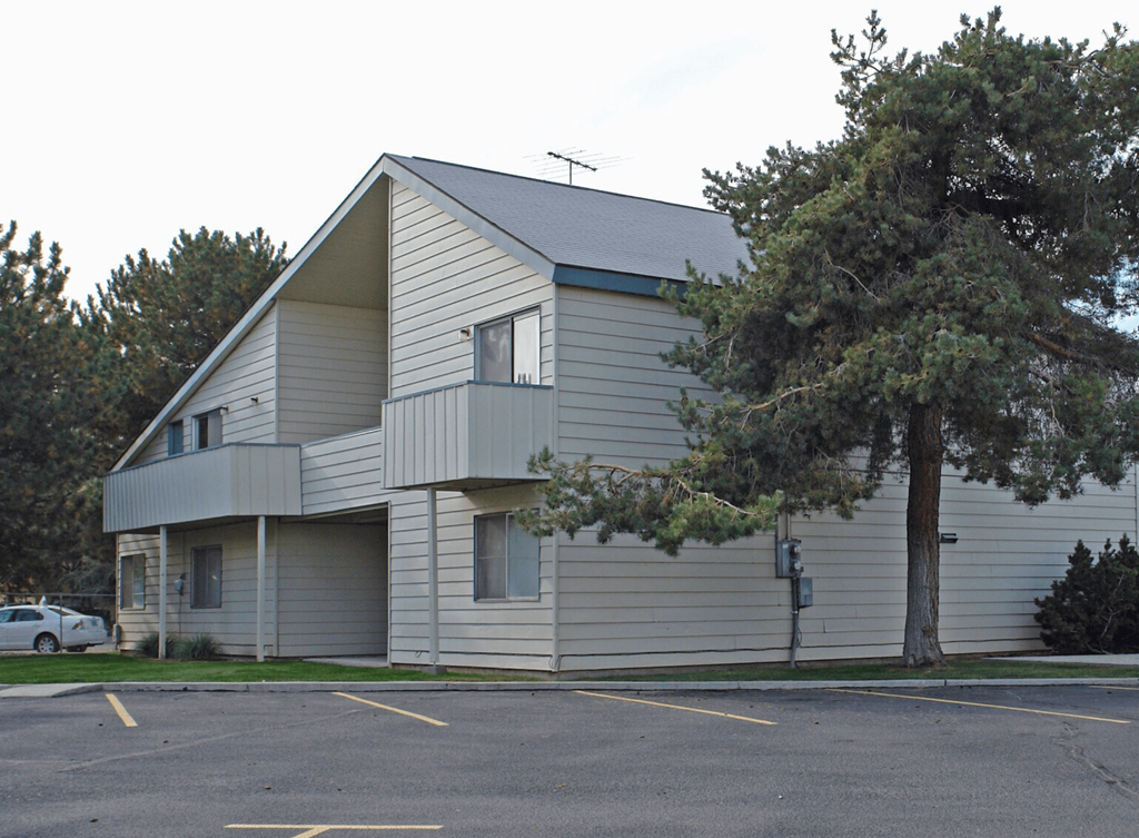 A grey building with a parking lot in front.