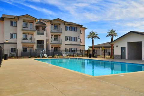 A swimming pool in front of a building with a fence and palm trees.