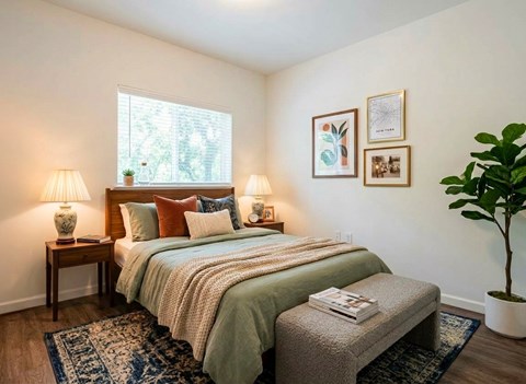 A bedroom with a bed, two lamps, a bench, and a potted plant.