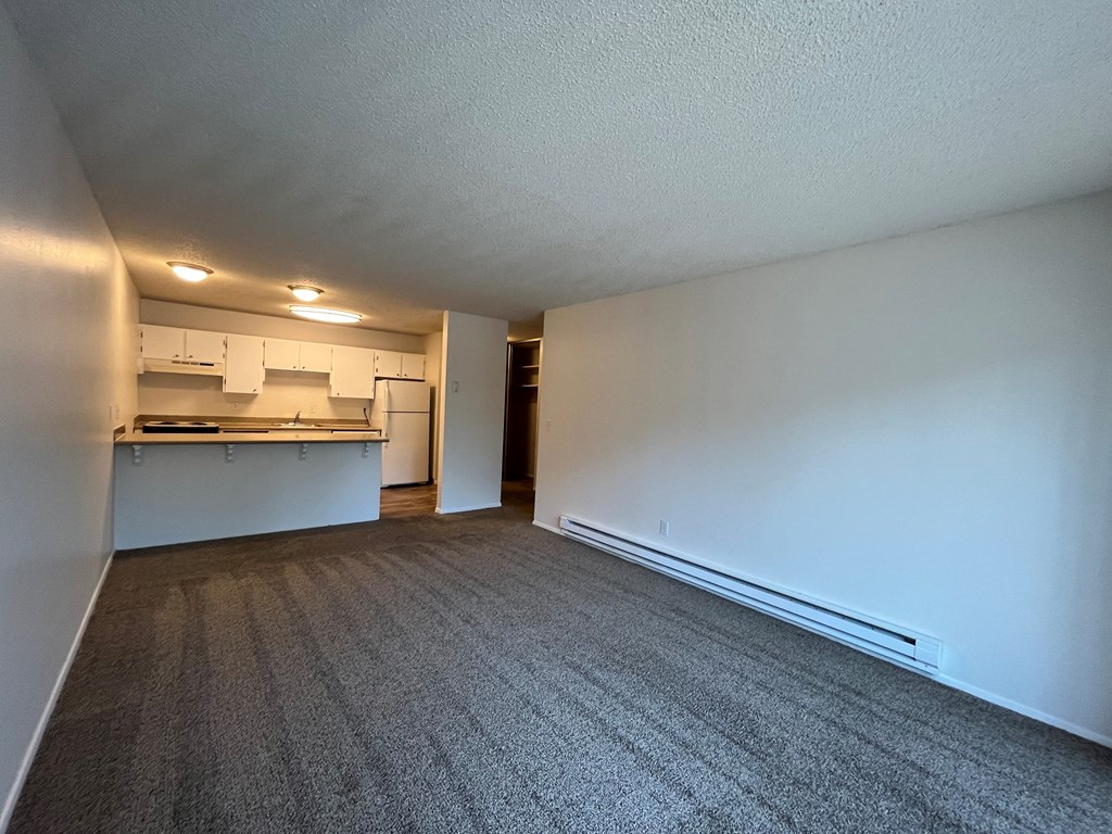 an empty living room with a kitchen in the background