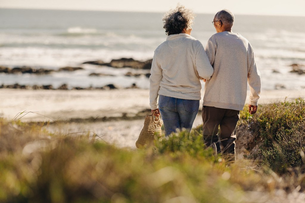 An elderly couple walking hand in hand on a beach.