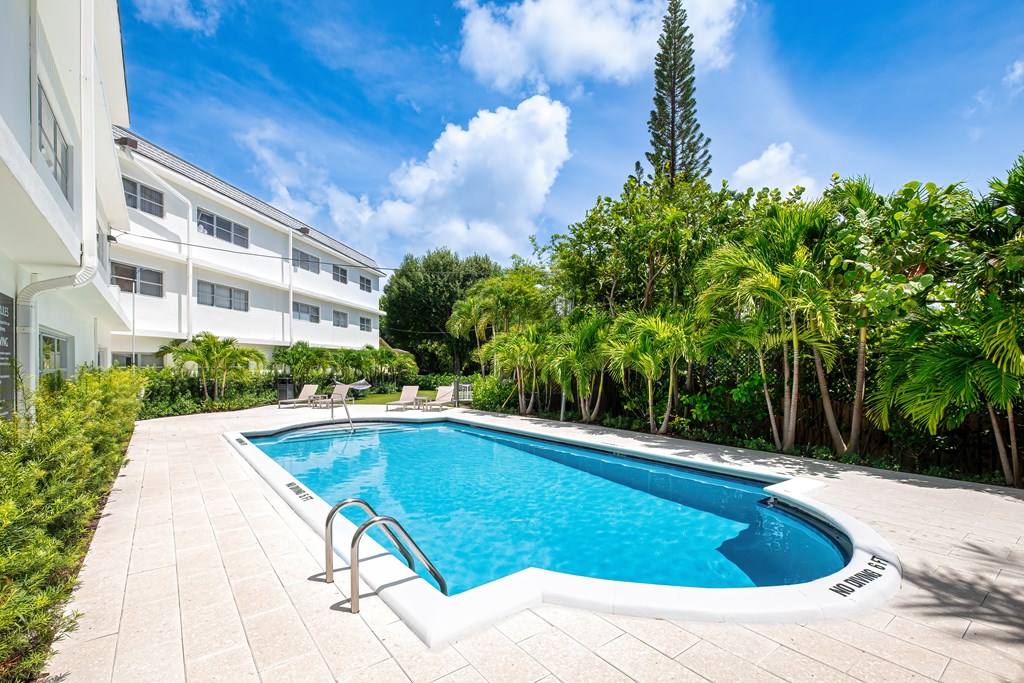 A small pool surrounded by trees and a white building.