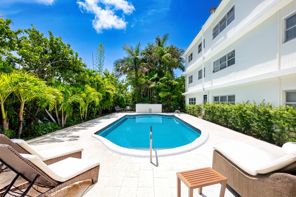 A pool surrounded by trees and chairs.
