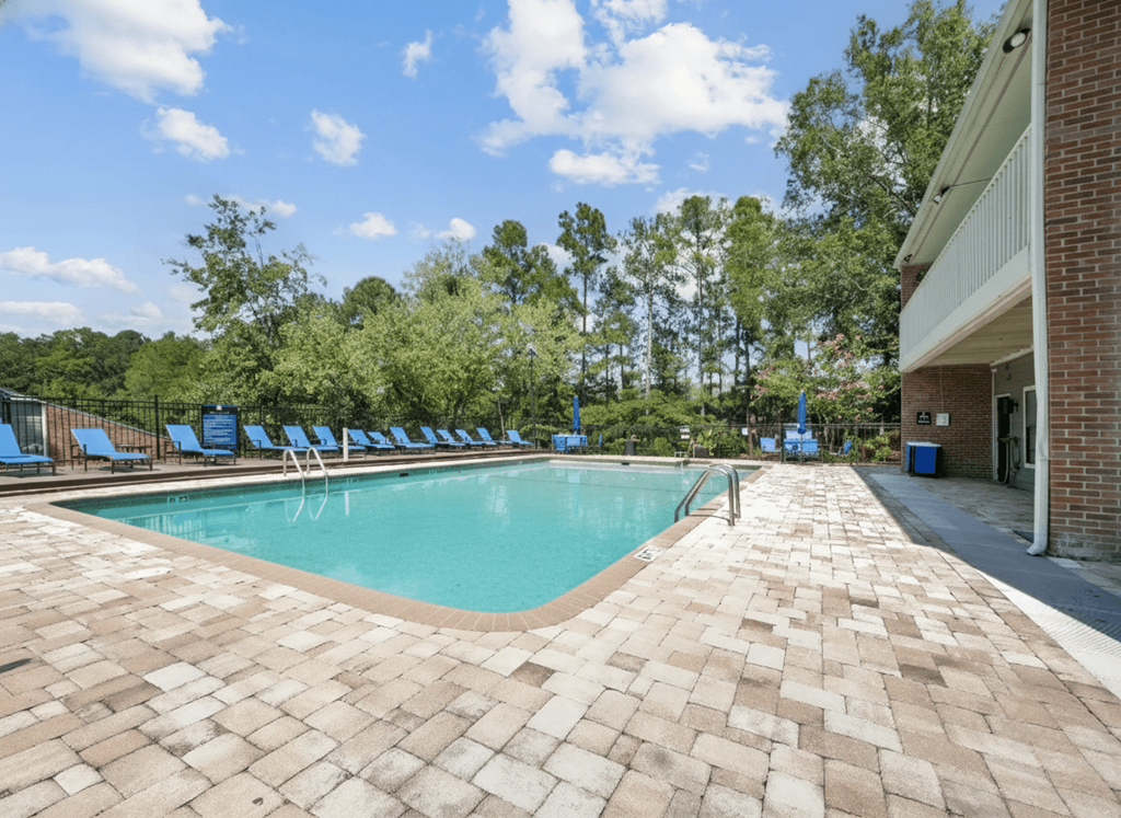 A large outdoor swimming pool surrounded by a brick patio and lounge chairs.