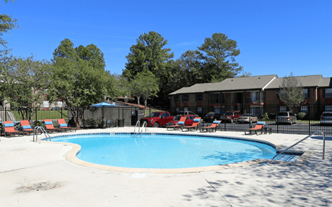 A swimming pool surrounded by trees and a building in the background.