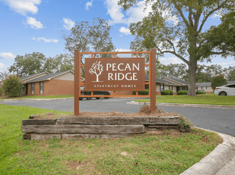 A sign for Pecan Ridge Apartment Homes is in front of a building.
