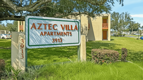 A sign for Aztec Villa Apartments stands in front of a building.