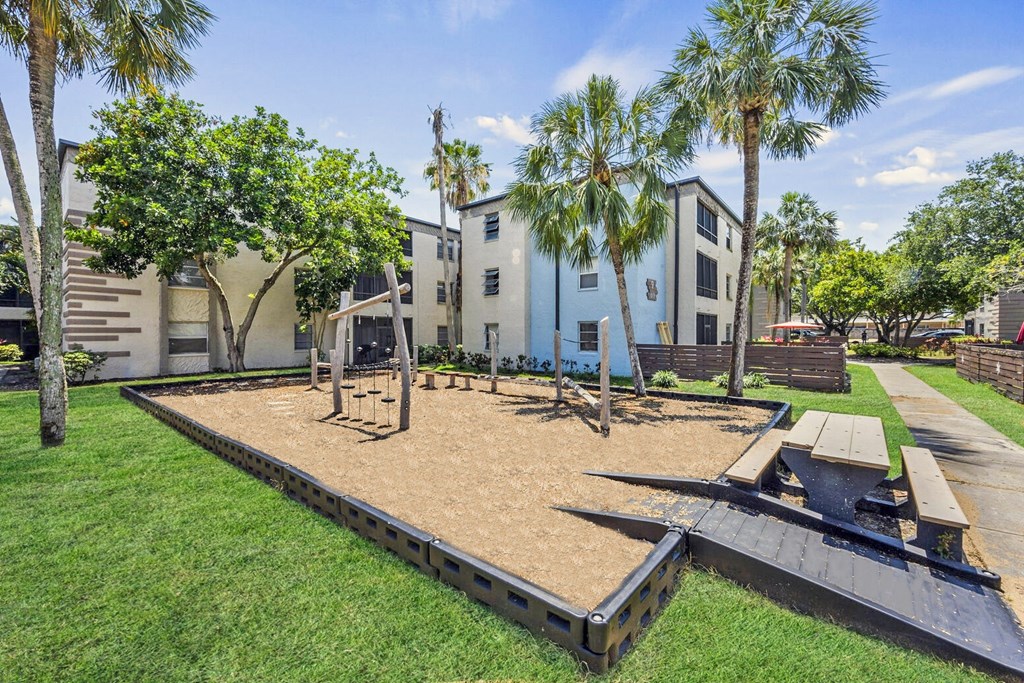 A playground with a slide and a picnic table is surrounded by palm trees.