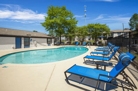 A pool with blue lounge chairs and a fence.