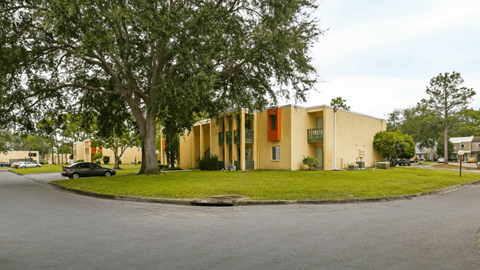 A yellow building with a red door is surrounded by trees.